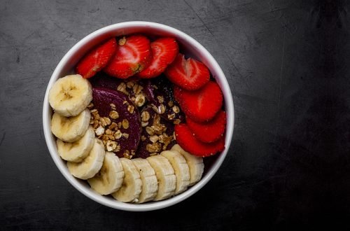 A high angle closeup shot of a white bowl with strawberry and banana slices